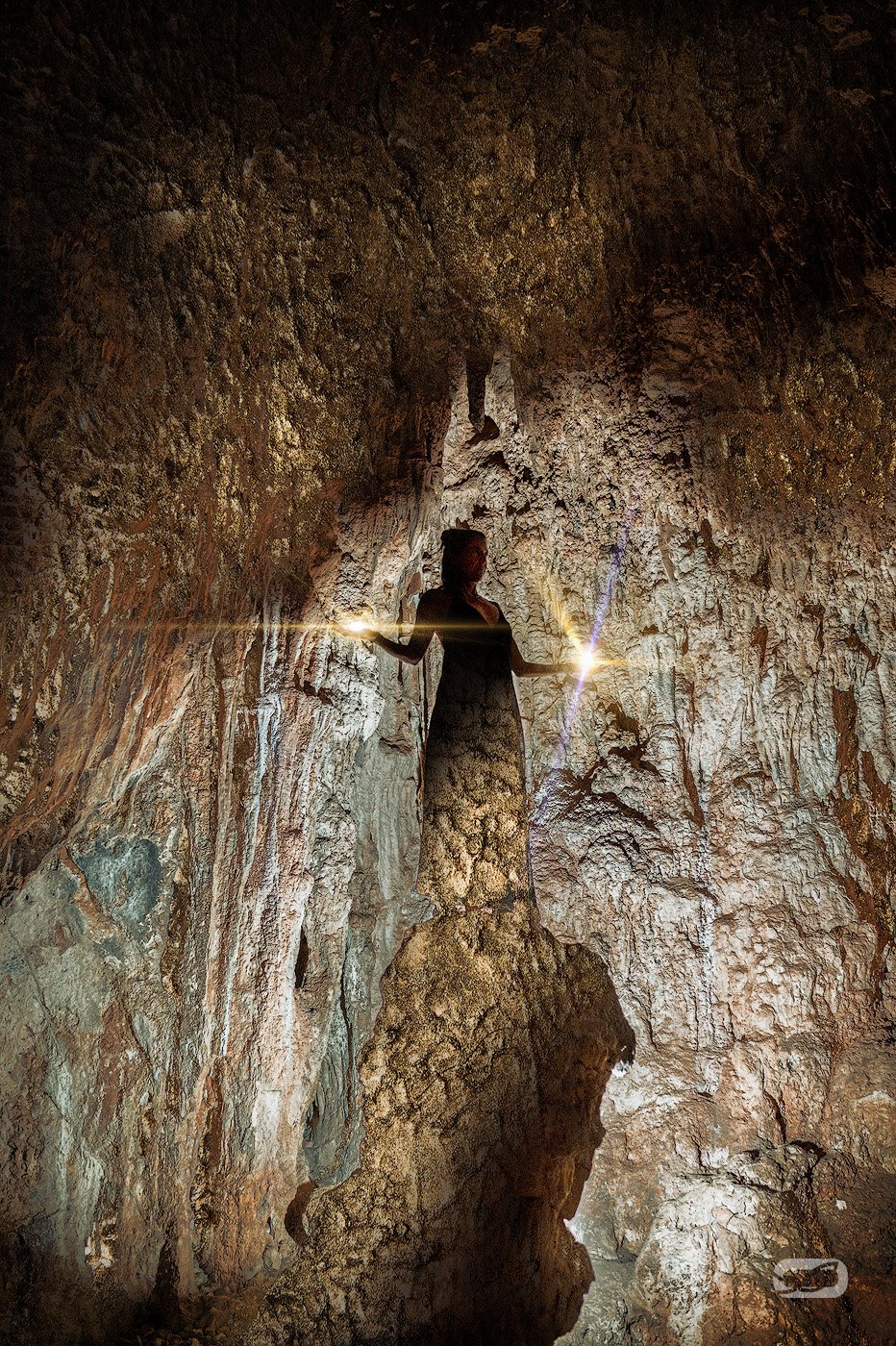 Eine Frau steht in einer schwach beleuchteten Höhle, die von einer einzigen hellen Lichtquelle erhellt wird. Die rauen, strukturierten Wände und die Decke der Höhle umgeben die Figur. Die Szene hat eine ätherische und geheimnisvolle Atmosphäre, als ob sie von Zauber und alter Magie berührt wäre.